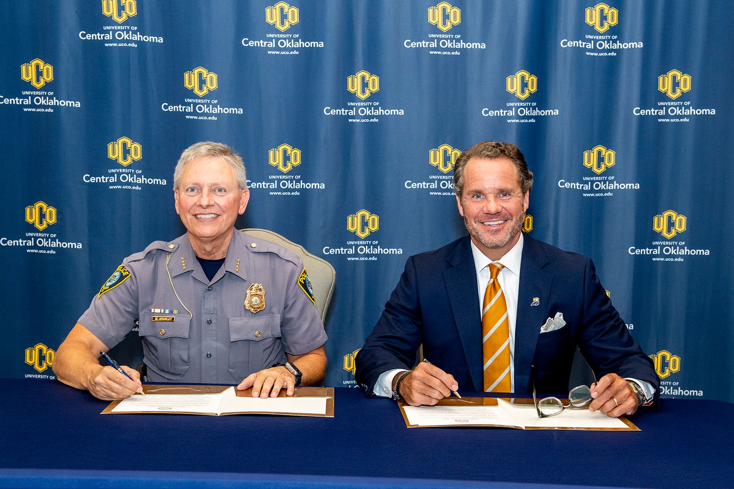 Two individuals pose for a photo while signing a document.